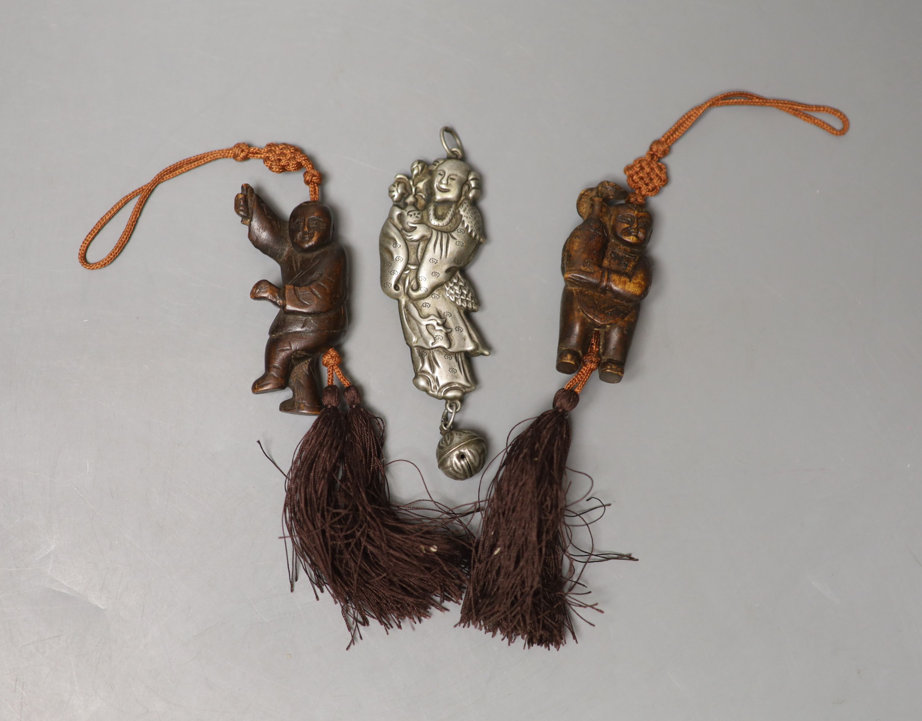 A Chinese metal baby's rattle and two carved wood figural pendants